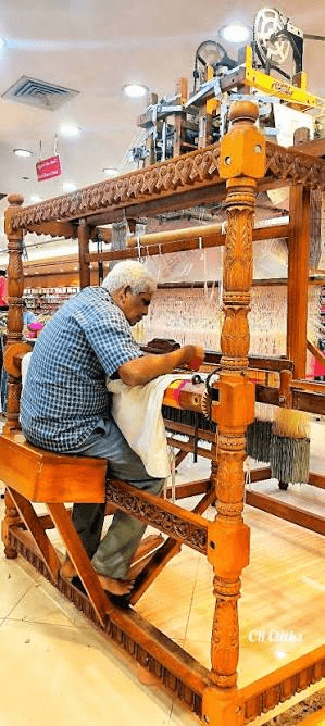 A weaver seated at a carved wooden handloom, working on a saree